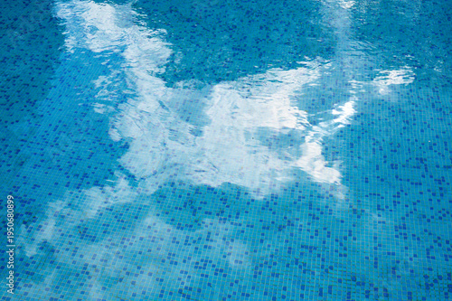 Blue swimming pool water surface with white clouds reflection in natural sunlight