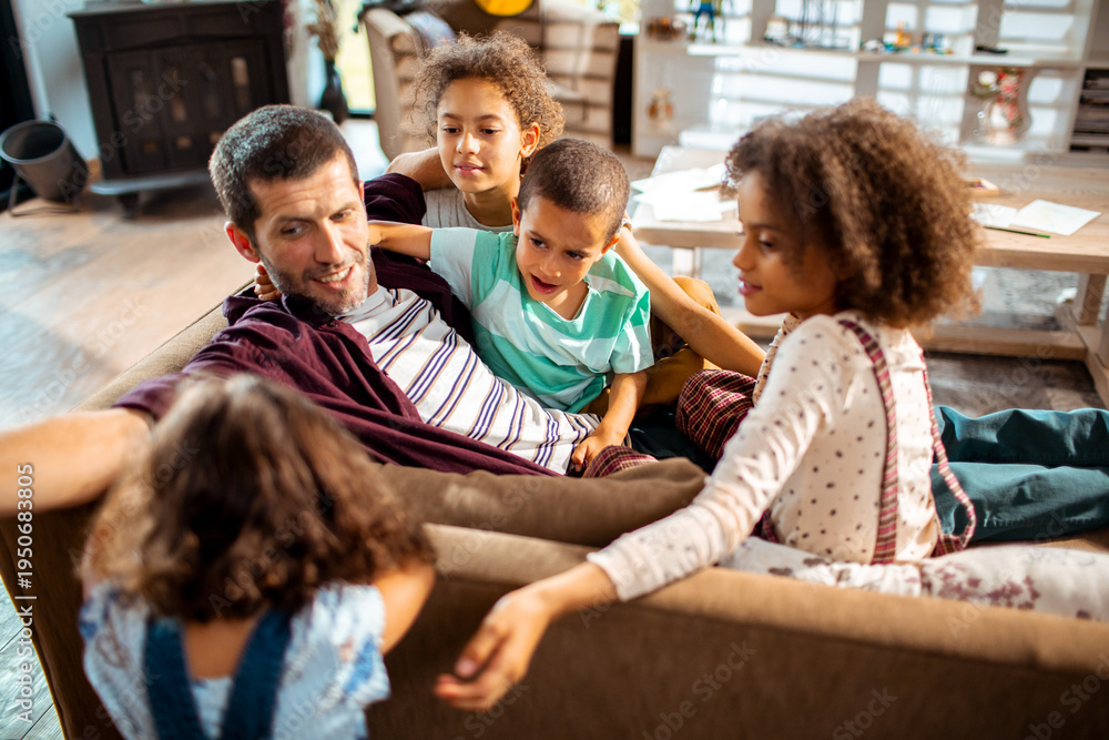 Obraz premium Father bonding with four children on living room sofa at home