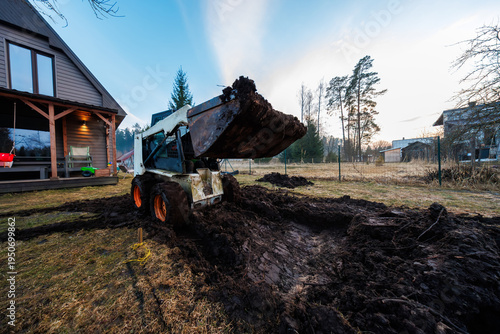 Skid Steer Digs Trench Beside Modern A Frame Cabin at Sunset