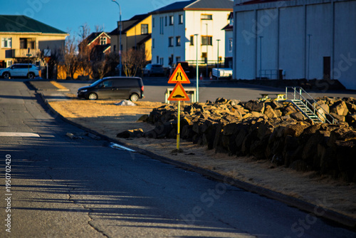 Warning traffic signs for road narrowing and speed bumps on a quiet suburban street in Iceland during golden hour