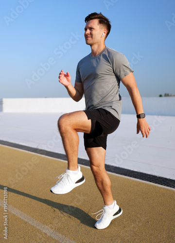 Energetic man training with high knees on an outdoor athletic track under a bright clear blue sky in daytime