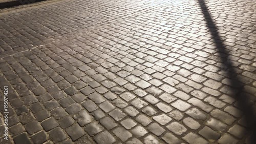 Old cobblestone pavement surface with sunlight and diagonal shadow in slow motion.