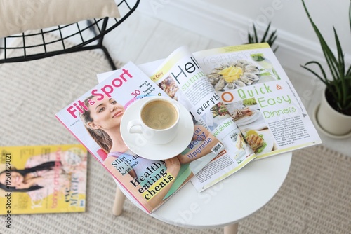Lifestyle magazines and cup of coffee on white table indoors, closeup