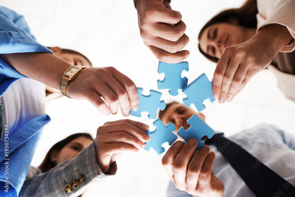 Obraz premium Team building. Group of businesspeople putting puzzle pieces together against blurred white background, bottom view