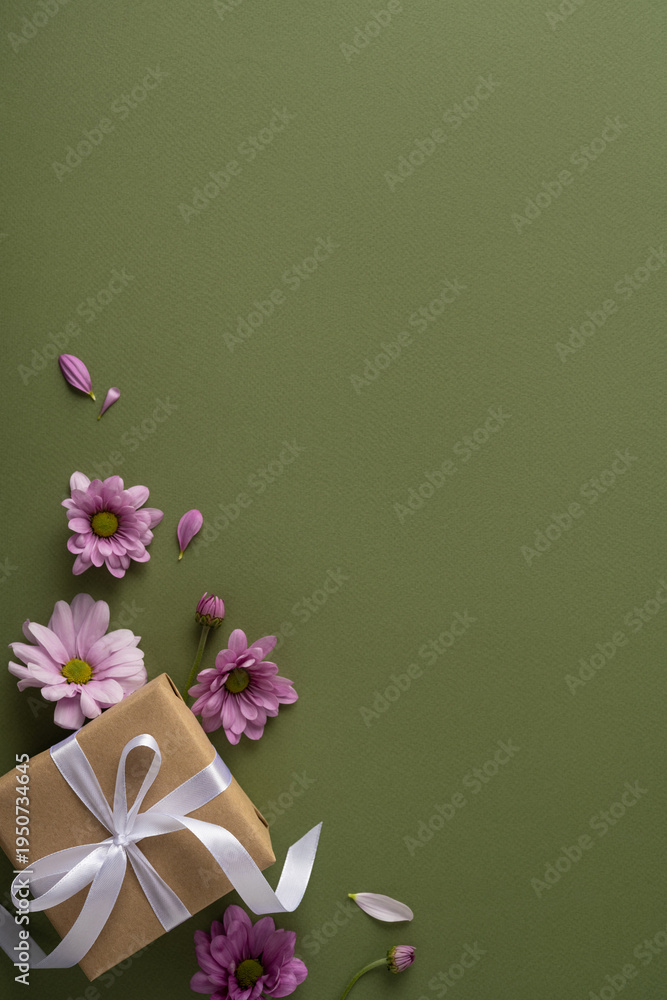 Obraz premium Happy Mother's Day vertical arrangement featuring a wrapped gift with white ribbon, pink daisies and scattered petals on an olive textured background evoking gratitude, love and spring celebration