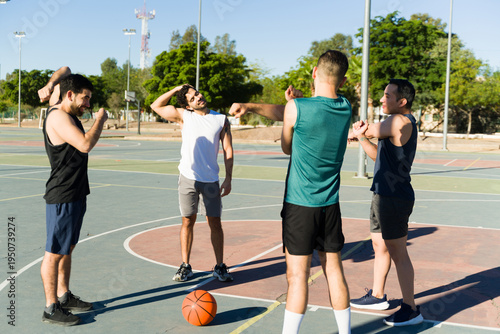 Four men warming up by stretching their arms and shoulders before a game or workout on a sunny outdoor court