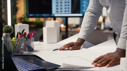 Tableau sur toile African american contractor examining architectural blueprints plans on table, review zoning regulations for construction project approval