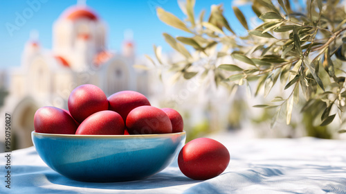 Red dyed Easter eggs arranged in a bowl on a table with a blurred church and olive branches in the background