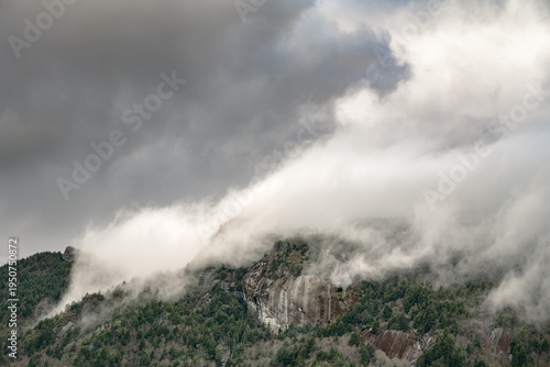 Schilderij op canvas Dramatic clouds rolling over forested mountain ridges with exposed rock faces in