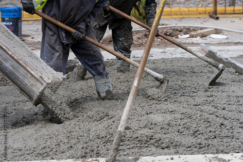 Cuadro en lienzo Construction workers pour wet cement onto a busy city street during daytime