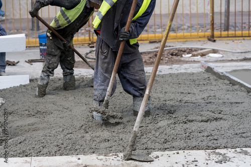 Schilderij op canvas Construction workers pour wet cement on a busy city street during daytime
