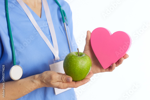 Close-up of a healthcare provider in scrubs holding an apple and a heart shape, focusing on the visual cues of medical expertise and nutritional guidance.