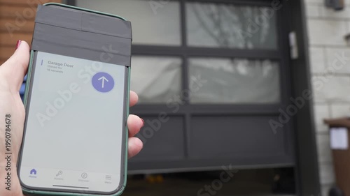 Hand holding smartphone displaying garage door control interface, showing gradual opening of garage door with interior tools and equipment visible