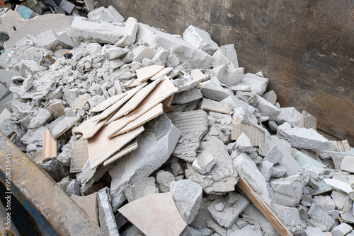 Construction waste from a renovation site and demolition debris concept in a metal container. Broken ceramic tiles and concrete chunks lie in a dumpster.