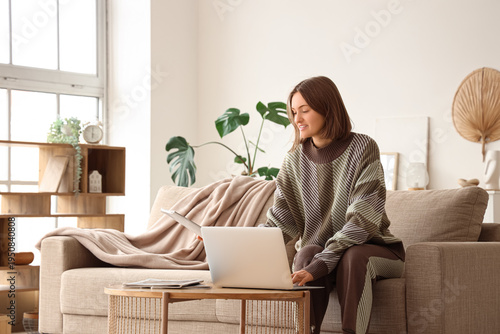 Beautiful young woman using modern laptop on sofa in living room