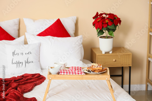 Tasty breakfast with waffles and Christmas plant poinsettia in bedroom