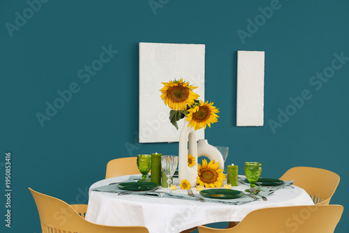 Modern table setting with sunflowers in vase near blue wall in room