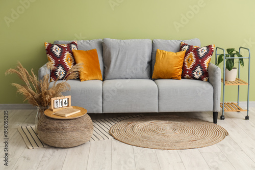 Interior of minimalistic living room with grey cozy sofa, houseplant and pouf
