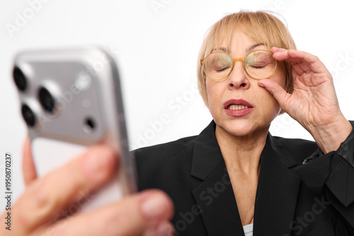 Fotografie Mature woman wearing glasses and black blazer holds smartphone close to face, eyes closed and touching glasses