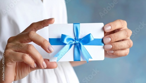 A woman's hands gently hold a small wrapped Christmas gift box decorated with a beautiful ribbon bow for a holiday celebration surprise