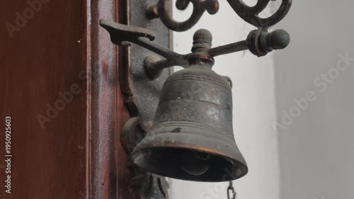 Close-up of an antique bronze bell mounted on a dark wooden pillar, showing rustic texture and traditional craftsmanship.