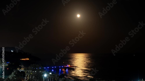 Timelapse Moonlight Over Sea Waves Full Moon Glow ocean waves on sandy beach at night wooden pier. The moon illuminates water surface. Concept of beach vacation slowing down on seacoast. Travel