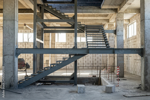 Interior of a building construction site featuring a metal staircase, concrete columns and industrial framework.