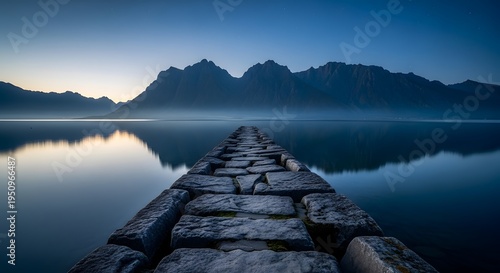 Stone pier extending into a calm lake at twilight with mountain reflections