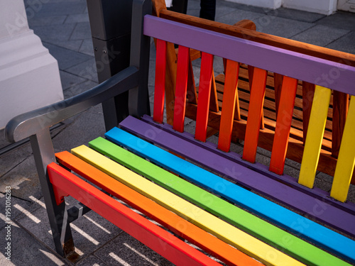 Close up of colorful rainbow bench with wooden slats in sunlight, urban outdoor furniture symbolizing diversity, inclusion and modern city design.