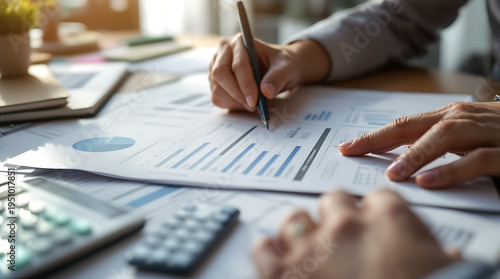 A person's hands are shown analyzing financial documents with a calculator and pen on a desk.