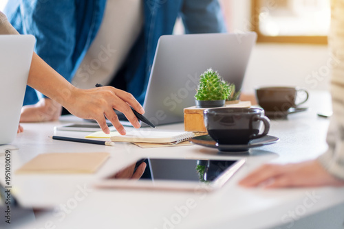 A group of people working together at a modern office desk with laptops and coffee