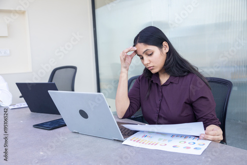 Young indian businesswoman or employee having stress and burnout while reviewing financial documents laptop in office. Workload, deadline. Mental health . Difficult task.