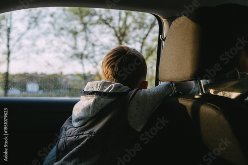 A child in a car is looking out the window without a seat belt