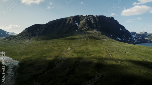 Cinematic drone shot flying sideways and forward towards the massive Blahoa mountain. View of the green tundra and lake Blåhøtjønna in the Trollheimen range, Oppdal, Norway. Sunny summer day