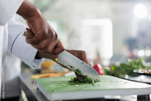 Fotografie Close up of african american hands using professional knife to chop finely fresh organic herbs and vegetables for stew recipe