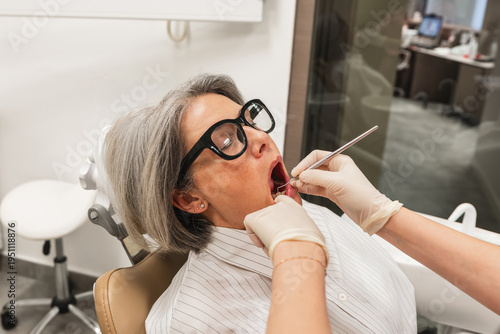 Mature woman undergoing an oral examination by a dentist in a modern dental office, focusing on preventative healthcare