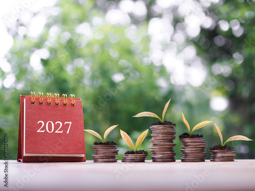 2027 desk calendar, Plants growing up on stack of coins. The concept of saving money, Financial, Investment and Business growing in new year 2027