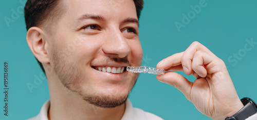Young man smiling while holding a clear dental aligner for orthodontic teeth straightening