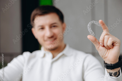 Smiling man holding a clear dental aligner demonstrating invisible braces for modern orthodontic treatment