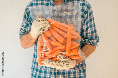 Close-up of farmer carrying plastic bag filled with fresh carrots, farming and vegetable harvest concept