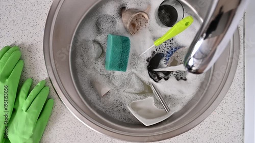 A top view of a kitchen sink with dirty dishes in a home interior. Water flows from an open faucet.