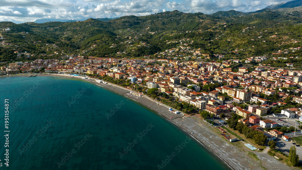 Fototapeta premium Panorama of a vibrant coastal town curving along a deep blue bay. Dense buildings sit between a long beach and green hills. Aerial view of seafront of Sapri, in province of Salerno, Campania, Italy.