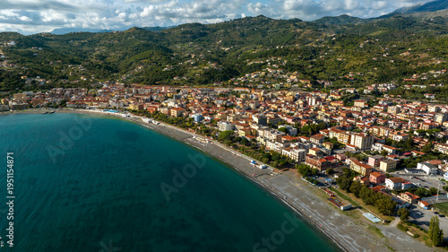 Panorama of a vibrant coastal town curving along a deep blue bay. Dense buildings sit between a long beach and green hills. Aerial view of seafront of Sapri, in province of Salerno, Campania, Italy.