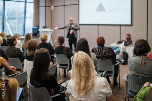 Business presentation with speaker engaging attentive audience in modern conference room, networking, learning, collaboration.