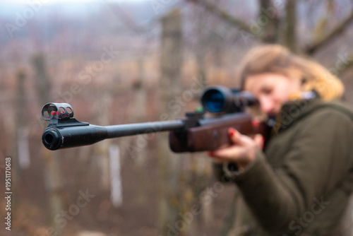 фотографія A woman is poised to shoot, aiming a rifle steadily towards her target in a natural setting