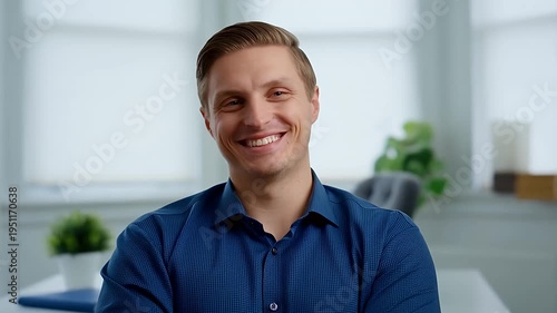 Man smiling sincerely with folded arms in office background, happy employee at work, positive professional.