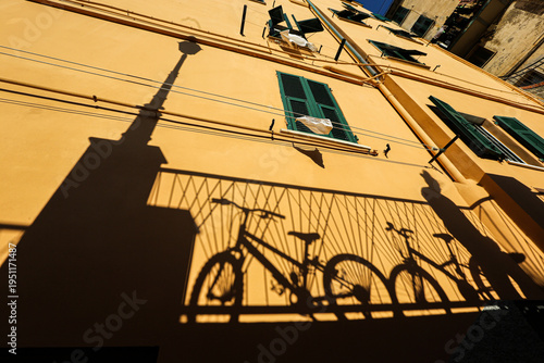 bicycle shadow, striking bicycle shadow cast on a bright yellow building facade with green shutters