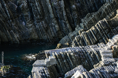 layered rock formation, dramatic layered rock formation plunging into dark sea water