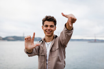 Smiling young man showing hand signs against sky
