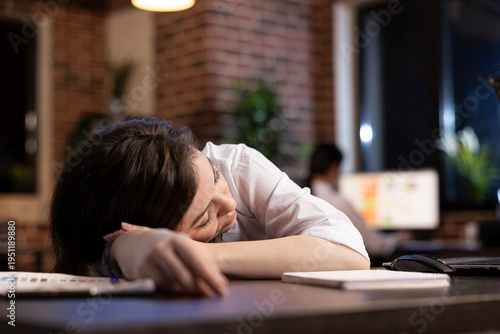 Fotografie Tired businesswoman takes powernap at her workstation, resting briefly amid her demanding schedule in late night office setting
